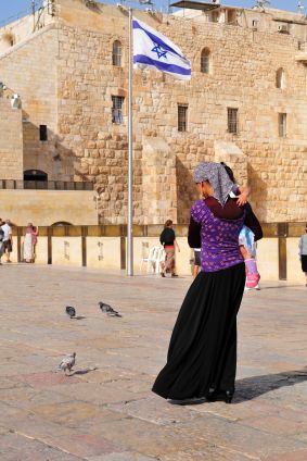 An Orthodox Jewish woman carries her child across the Promenade in front of the Kotel