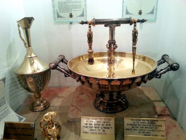 The tall jug contains enough menorah oil for all seven lamps. That oil is poured into the smaller gold jug (bottom left) that is used to replenish the individual lamps. The bowl with the tongs and brush is for cleaning the Menorah. Menorah Oil-Golden Oil Flask-Vessels