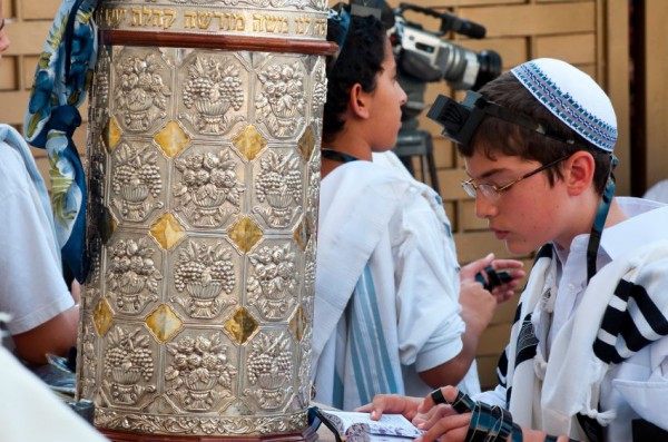 A young man recites prayers with a straps on his hand and the small leather black box on his forehead (tefillin) kotel-tefillin-Torah-bar mitzvah