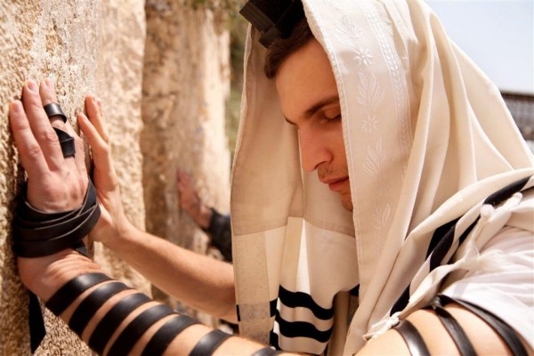 An Israeli man prays at the Western (Wailing) Wall in the Old City of Jerusalem, wearing a tallit (prayer shawl) and tefillin (phylacteries). Israeli man prays Western (Wailing) Wall Old City of Jerusalem tallit prayer shawl tefillin phylacteries