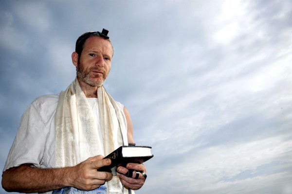 A Jewish man with a siddur (prayer book) wears tefillin (phylacteries) and a tallit (prayer shawl) during morning prayer. A Jewish man prepares to recite morning prayer.