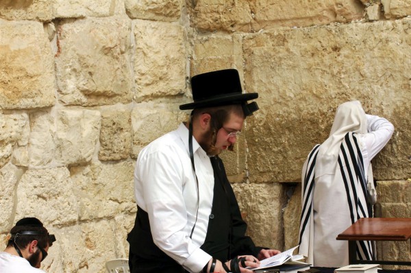kotel-men-prayer An Orthodox Jewish man prays at the Western (Wailing) Wall using a siddur (Jewish prayer book). The box and black straps are tefillin (phylacteries), which are put on during morning prayer.