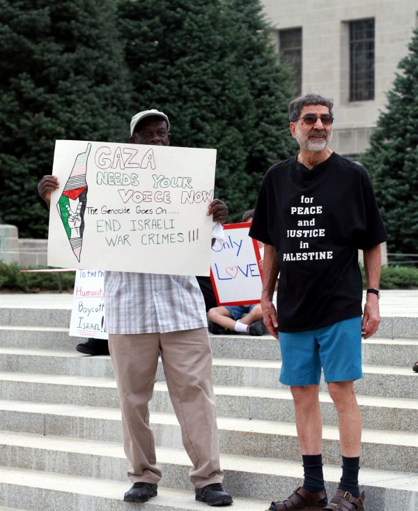 An anti-Israel protester holds a sign falsely accusing Israel of genocide and war crimes. The map on the sign reveals the ambition to wipe out Israel and for a Palestinian state to replace it. The sign behind him on the left tells passersby to boycott Israel. An anti-Israel protester holds a sign falsely accusing Israel of genocide and war crimes. The map on the sign reveals the ambition to wipe out Israel and for a Palestinian state to replace it. The sign behind him on the left tells passersby to boycott Israel.