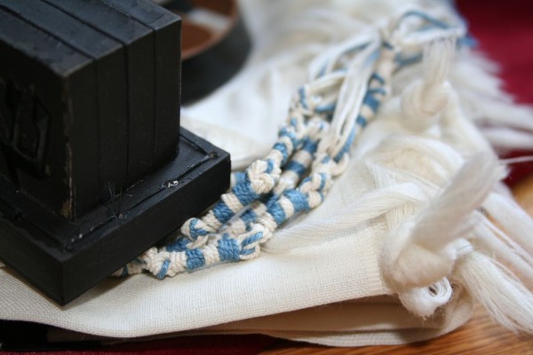 The black box of tefillin (which contains Scripture) and the tzitzit with the tekhelet (blue thread) of the tallit. The black box of tefillin (which contains Scripture) and the tzitzit with the tekhelet (blue thread) of the tallit.