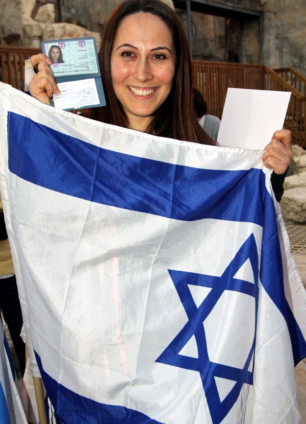 A woman holds up the Israeli flag and her new Israel identification after making Aliyah. (Jewish Agency photo by Brian Hendler) A woman holds up the Israeli flag and her new Israel identification after making Aliyah. (Jewish Agency photo by Brian Hendler)