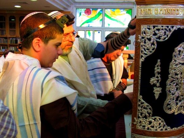 A Jewish 13-year-old male reads from a Torah scroll protected by an elaborately decorated Torah tik. A Jewish 13-year-old male reads from a Torah scroll protected by an elaborately decorated Torah tik.