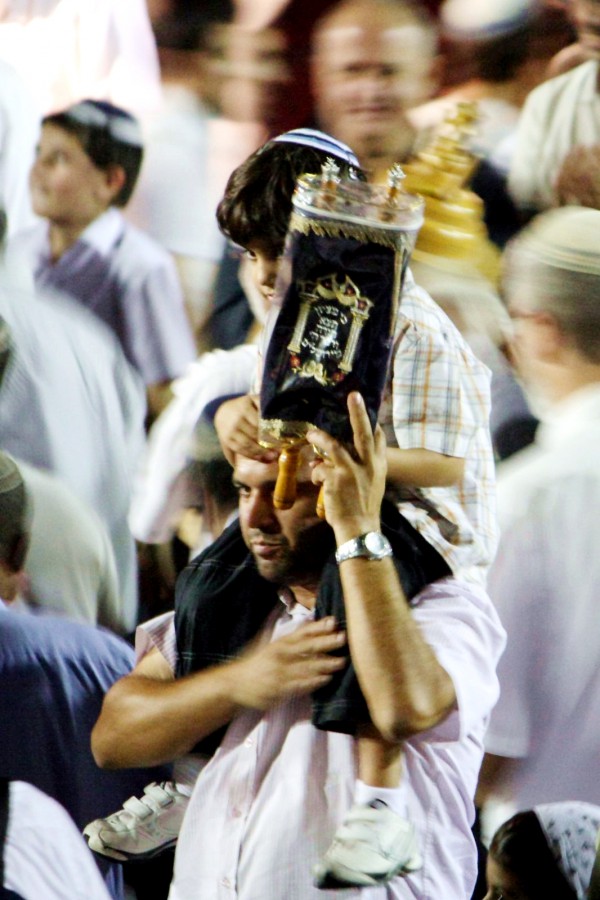 A father in the midst of a large crowd of people dancing and singing with the Torah carries his son on his shoulders as he parades a small Torah scroll on Simchat Torah. (Photo by Avital Pinnick) A father in the midst of a large crowd of people dancing and singing with the Torah carries his son on his shoulders as he parades a small Torah scroll on Simchat Torah. (Photo by Avital Pinnick)