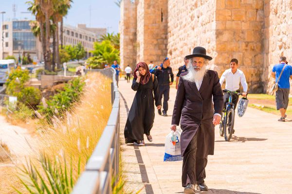 An elderly orthodox Jewish man walks with other Israelis and tourists outside the Old City walls of Jerusalem.